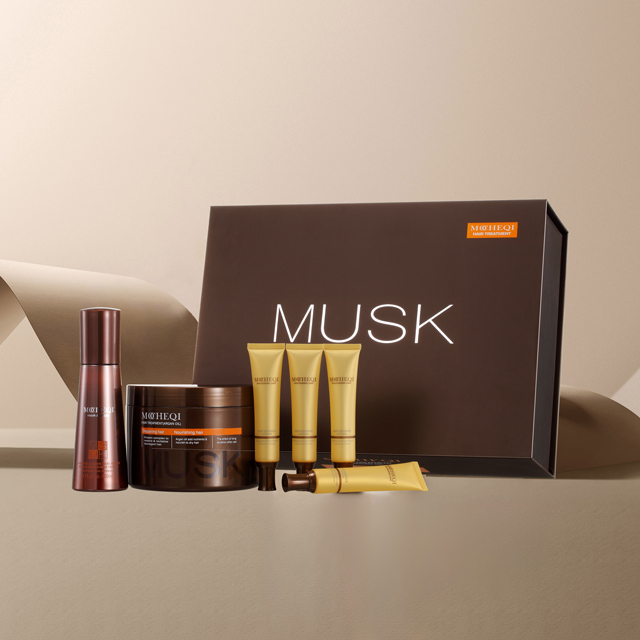 Zestaw kosmetyków do włosów MOHEQI MUSK, umieszczony na beżowym tle, z fragmentami ciemniejszego papieru w tle. Zestaw składa się z ciemnobrązowego pudełka z napisem "MUSK", dużego słoika z maską do włosów, buteleczki z szamponem oraz trzech mniejszych, złotych tubek.